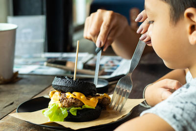 Cropped hand of mother and son eating food on table