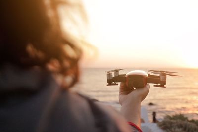 Rear view of woman holding drone at beach during sunset