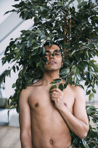 Shirtless man with eyes closed standing by plant at home