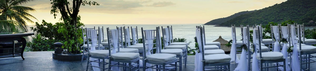 Chairs and table by sea against sky during sunset