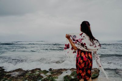 Rear view of woman standing at beach against sky