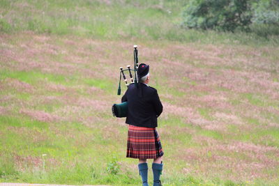 Rear view of bagpiper standing on grassy field