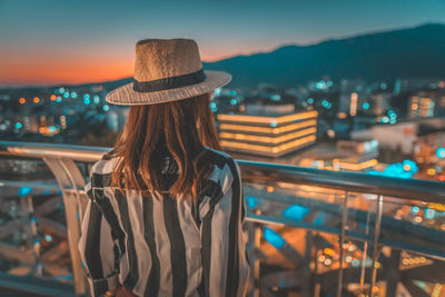 Rear view of woman standing against illuminated cityscape