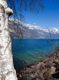 Scenic view of sea by mountain against blue sky