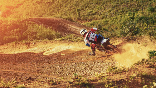 Rear view of biker riding motocross on dirt road