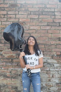 Young woman with guitar standing against brick wall