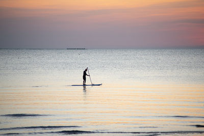 Silhouette man surfing in sea against sky during sunset