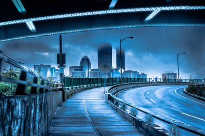 Illuminated bridge and buildings against sky at dusk