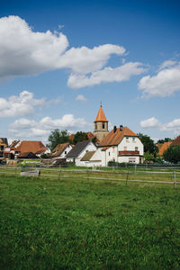 Houses on field by buildings against sky