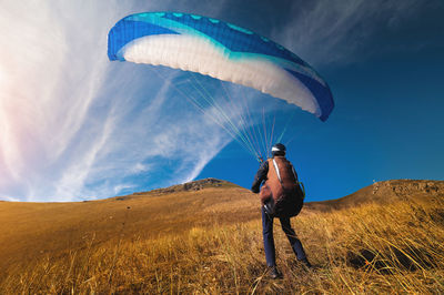 Paraglider stands on yellow grass in a field and holds his parachute in the air. extreme sport