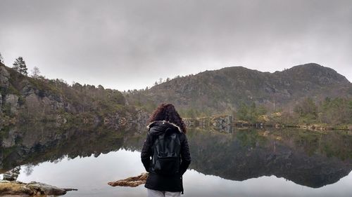 Rear view of woman standing by lake against sky