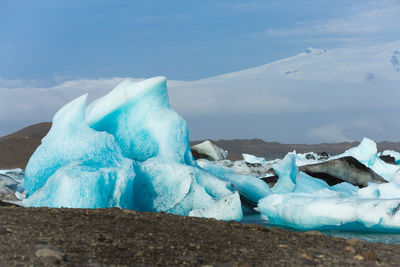 Blue ice floating on snow covered landscape against sky