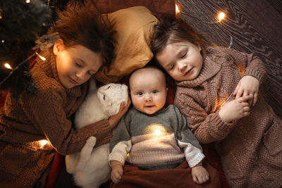 Three children with a domestic cat and a garland are comfortably resting