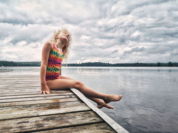 Woman sitting on pier over lake against sky