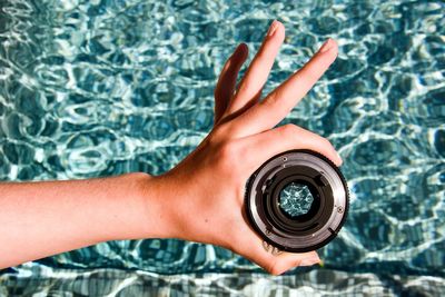 Cropped hand of person holding lens against water at swimming pool