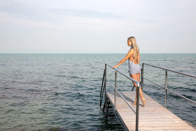 Woman standing on pier over sea against sky