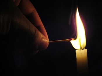 Close-up of hand lighting candle in the dark