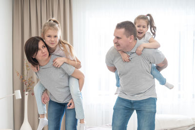 Father and mother piggybacking daughters at home