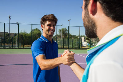 Male friends shaking hands while standing on tennis court