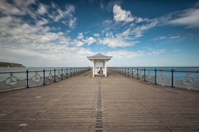 Woman sitting on built structure on bridge against sky