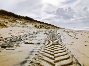 Tire tracks on sand at beach against sky