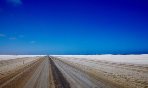 Road amidst land against clear blue sky