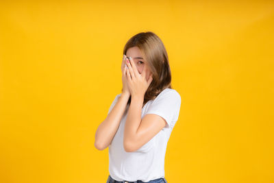 Portrait of young woman standing against yellow background