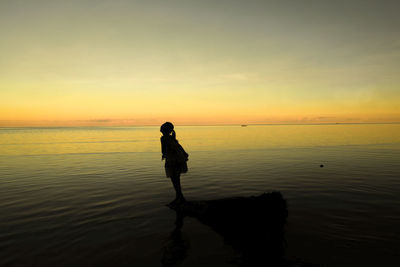 Silhouette man standing on beach against sky during sunset