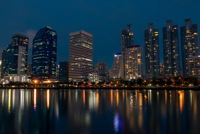 Illuminated buildings by river against sky at night