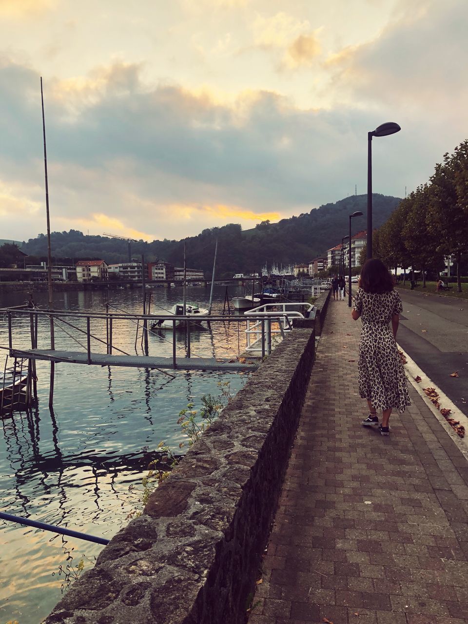 REAR VIEW OF WOMAN WALKING ON SHORE DURING SUNSET