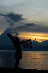 Silhouette girl standing on beach against sky during sunset