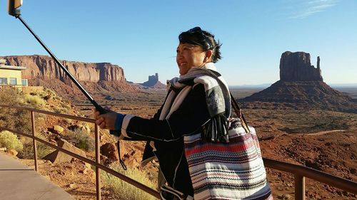 Smiling woman clicking selfie while standing on mountain against sky