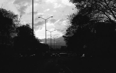 Silhouette of trees and road against cloudy sky