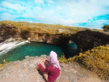 Woman sitting on mountain by sea against sky