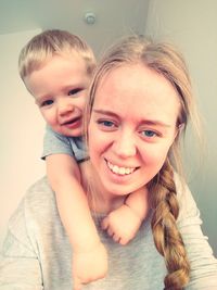 Portrait of happy mother giving piggyback ride to son at home