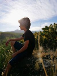 Side view of woman sitting on field against sky