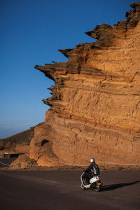 Man riding motor scooter by rock formation against sky