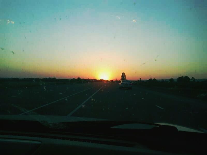 transportation, sunset, mode of transport, car, land vehicle, road, vehicle interior, sky, windshield, orange color, on the move, glass - material, transparent, sun, travel, landscape, silhouette, road marking, car interior, no people