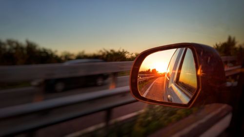 Close-up of side-view mirror against sunset sky