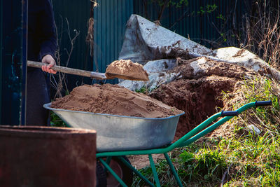 Man uses shovel and fills wheelbarrow with sand. construction works close-up. rural life 
