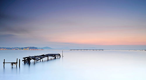 Old pier on sea against sky at sunset