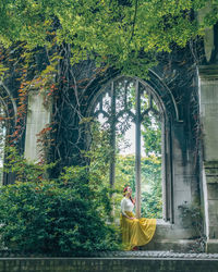 Woman sitting by trees against window