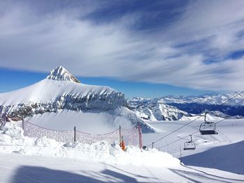 Ski lift by snowcapped mountain against sky