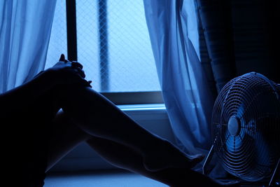 Low section of woman on bed by electric fan