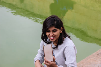 High angle view of woman taking selfie while sitting against lake