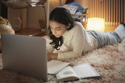 Girl doing homework with laptop on floor in her bedroom