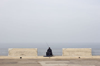 Rear view of person fishing at promenade against sky during foggy weather