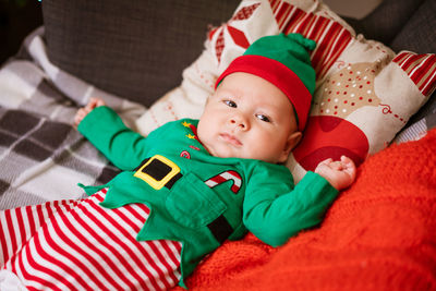 Beautiful half-year-old child lies on pillows and smiles in a red-green costume