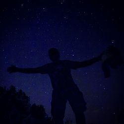 Low angle view of man with arms outstretched standing against star field at night