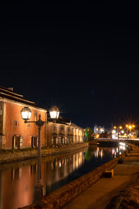 Illuminated buildings by river against sky at night